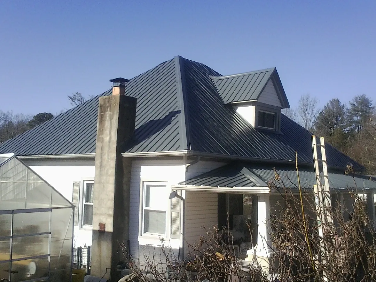 Dark blue standing seam metal roof on a white farmhouse with dormer in Ten Mile