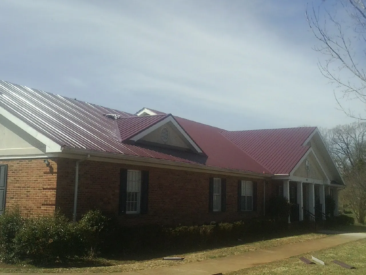 Red metal roof with gabled entries on a long brick building, from a Hail Damage Roof Repair job in Ten Mile