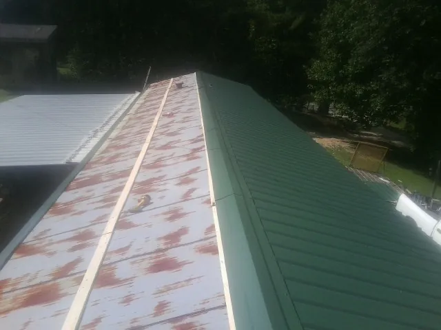Old rusted panels beside newly installed green metal roofing — Wind Damage Roof Repair by Roofing Brothers in Ten Mile