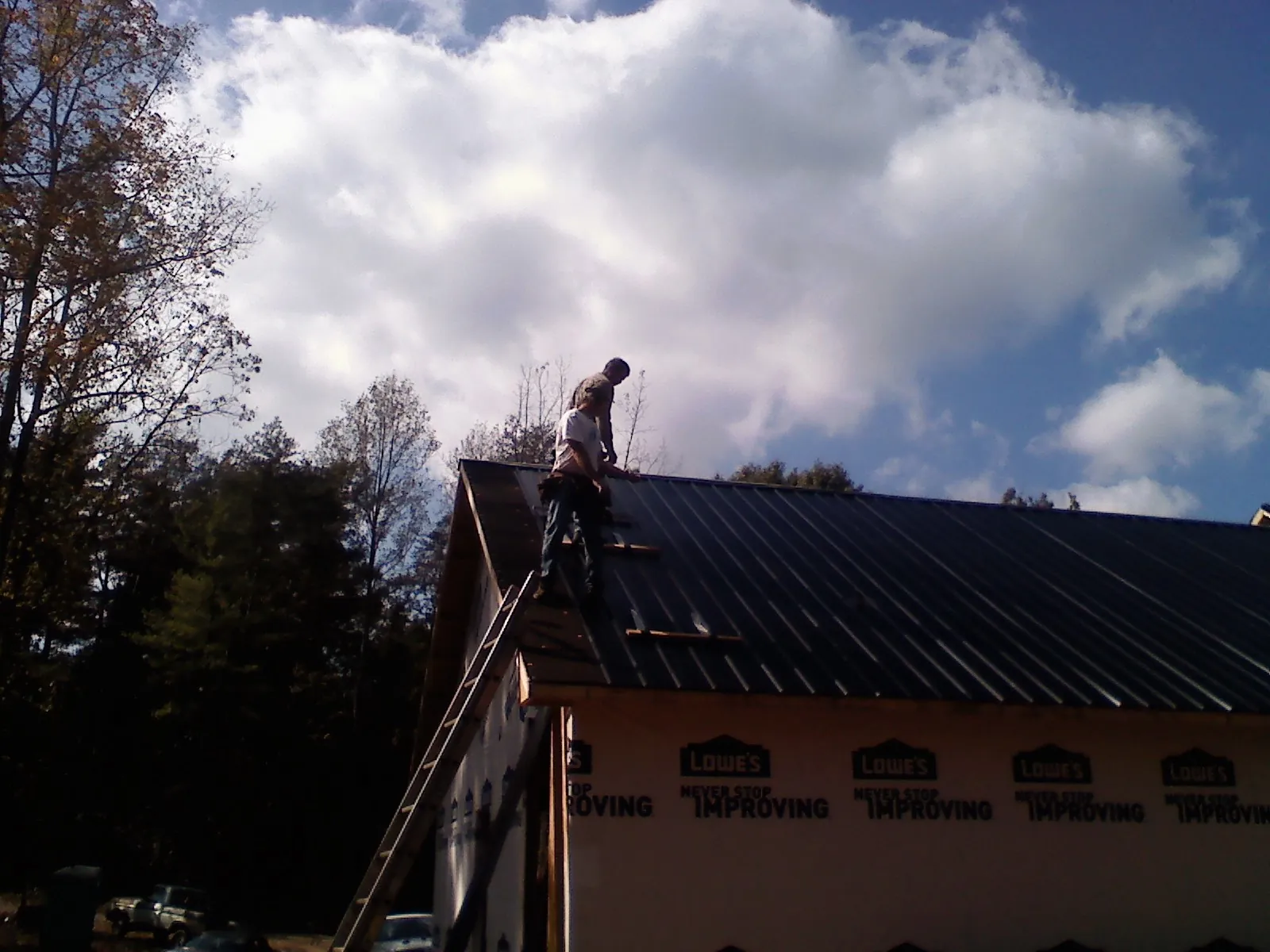 Roofer fastening dark metal panels high against a cloudy sky, from a Roof Inspection job in Ten Mile