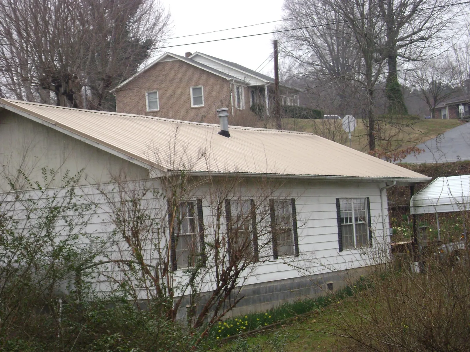 Tan metal roof on a white sided house set into a hillside — Commercial Roofing by Roofing Brothers in Ten Mile
