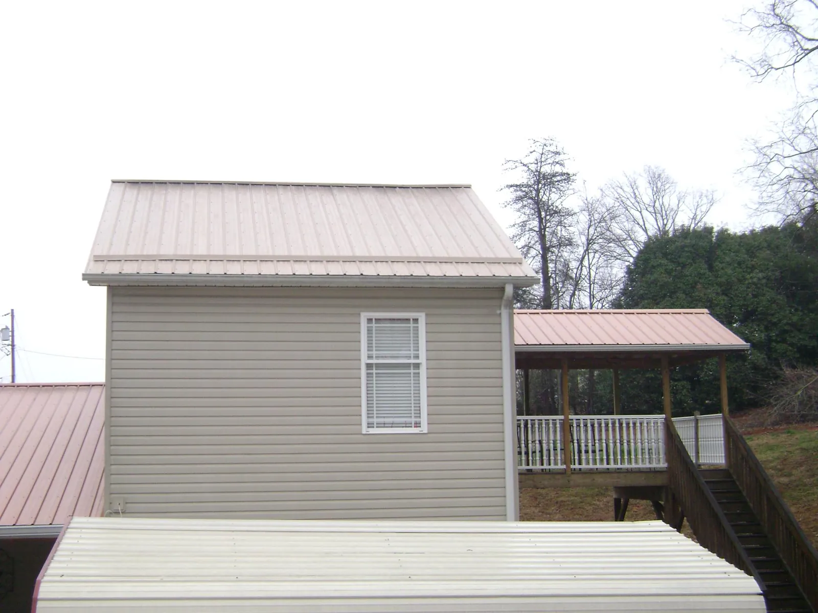 Tan metal roofs on a two story addition and attached porch, from a Roof Replacement job in Ten Mile